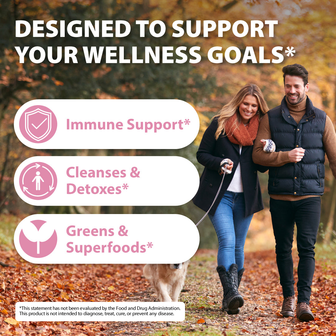 Promotional graphic with the text 'DESIGNED TO SUPPORT YOUR WELLNESS GOALS*' over a lifestyle photo of a couple walking a dog on a leaf-covered path in autumn. Three pink callout boxes list benefits: 'Immune Support*', 'Cleanses & Detoxes*', and 'Greens & Superfoods*'.